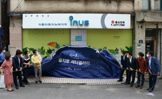 서울 중구 을지로동 주민센터에서 진행된 ‘을지로 셔터갤러리’ 개소식에 참석한 문동권 신한카드 경영기획그룹장(오른쪽 네 번째), 서양호 중구청장(다섯 번째) 등이 셔터를 덮은 천막을 걷어내고 있다. 사진=신한카드